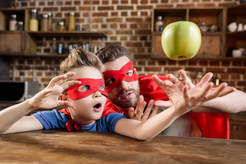 father and son in red superhero costumes playing with apple