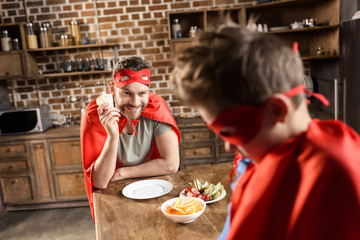 father and son in red superhero costumes eating in kitchen at home