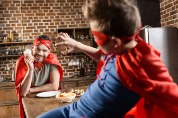 father and son in red superhero costumes eating in kitchen at home