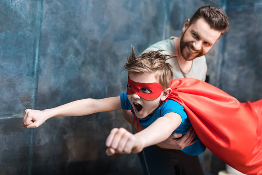 father holding son in superhero costume flying at home