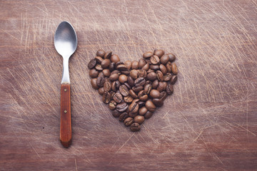 Heart shape made of coffee beans and cup over wooden background