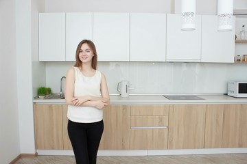 Fototapeta na wymiar Pretty young woman In a white T shirt standing in kitchen and smiling