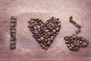 Heart shape made of coffee beans and cup over wooden background
