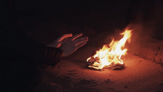 Hand of Young man seating near bonfire of burning shoes on the sand at coast strong bright flame summer dark night HD