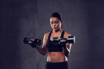young woman flexing muscles with dumbbells in gym