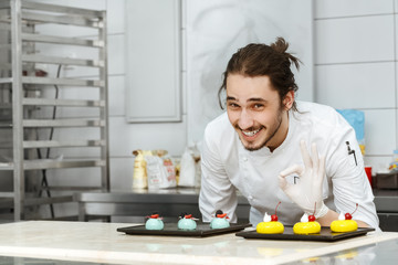 Cheerful chef posing with his cakes at the kitchen