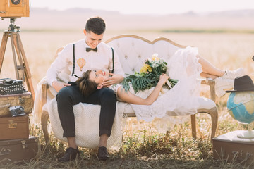 The happy groom with the wedding bouquet is lying on the groom`s laps and he is petting her face at...