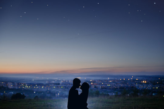 Silhouette Of A Couple In Love Against The Background Of A Night City, Stars And Horizon. Concept Is A Date On The Roof, The First Love