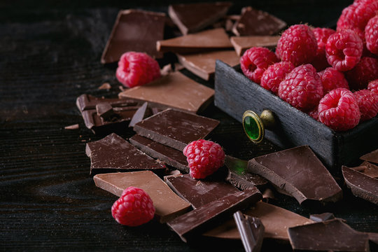 Dark and milk chopping chocolate and chips shavings chopping chocolate with fresh raspberries in black wood box over black burnt wooden background. Close up. Chocolate dessert concept