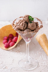 Cocktail glass with chocolate ice cream mini balls with fresh raspberries, mint and waffle cone on beige concrete texture background background. Dessert concept