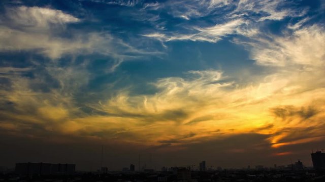Sunset time-lapse still featuring a colorful sky with feathery clouds and the silhouetted skyline of a city against the horizon