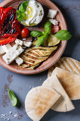 Ingredients for making pita bread sandwiches. Grilled vegetables, basil and feta cheese with flat bread on terracotta plate over gray texture background. Healthy fast food concept. Top view