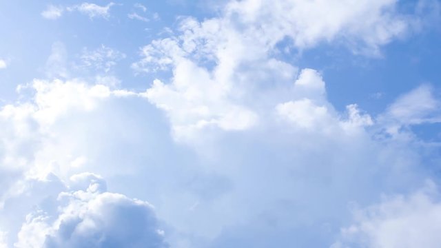 Time-lapse still of blue sky and clouds, showing a close-up view of the fluffy white formations drifting across a clear, bright background