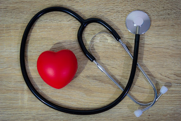 Stethoscope and red heart on wooden table background.