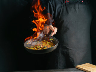 Cooking of vegetable mix stew with tossing on a hot frying pan in the tongues of flame. Colorful grains of corn and peas, asparagus and sweet peppers.