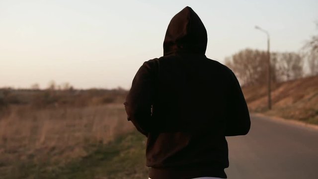 Lone runner at sunset outdoors in black hooded sweater. Slow motion