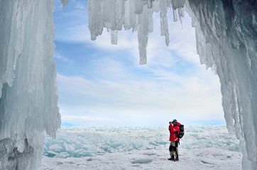 Турист фотографирует ледяные торосы на озере Байкал на фоне ледяного грота - obrazy, fototapety, plakaty