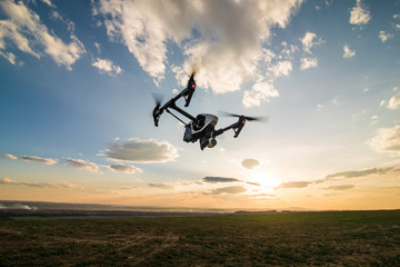 Fototapeta na wymiar White drone with digital camera flying in sky over field on sunset