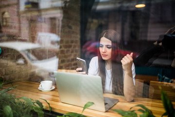 Young woman talking on the phone in front of laptop in coffee shop