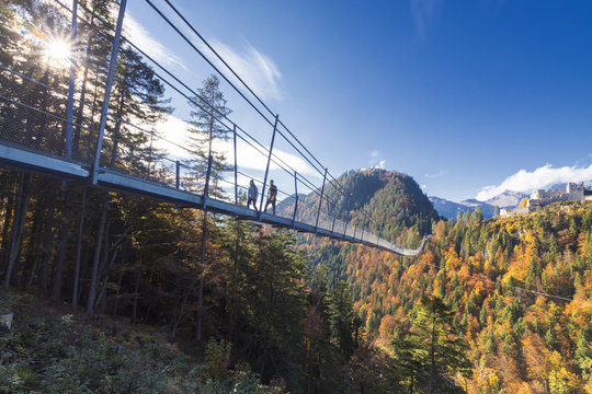 Tourists on the suspension bridge called Highline 179 framed by colorful woods in autumn, Ehrenberg Castle, Reutte, Austria