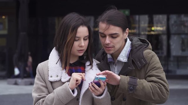 Young couple flipping the screen of a smart phone together at the street