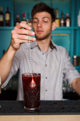 Young handsome barman pouring cocktail drink into glass
