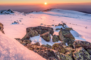 Pink sunset over frozen mountain top with rocks in the foreground