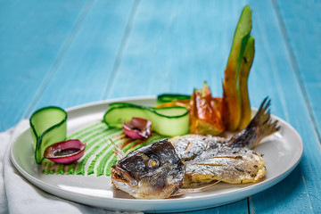 Fried fish dorado, decorated with cucumbers and onions. On a blue wooden background