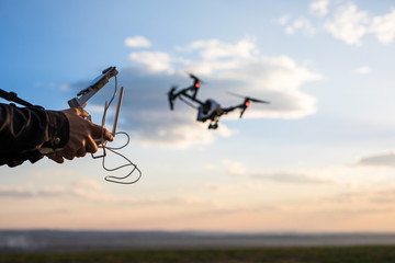 Demonstration of .copter Man controls quadrocopter flight. Flying the copter over a field over sunset sky. Remote control in a man's hands.