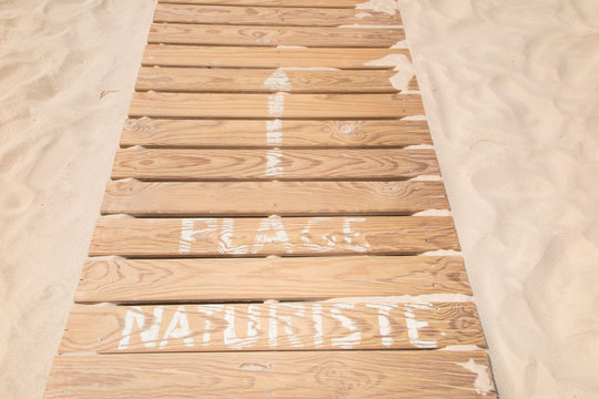 Wooden path to access the beach on which is written nudist beach