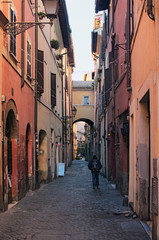 Fototapeta na wymiar A lonely tourist with a backpack walks along a narrow long street. Rome, Italy