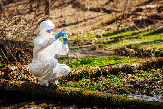Closeup of a female scientist examining the liquid contents of a conical flask in the forest.
