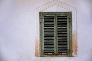Old green window with closed wooden shutters on an old white masonry