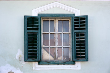 Old green window with open wooden shutters on an old mint green masonry