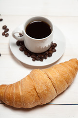 Cup of coffee and a croissant on a white wooden table