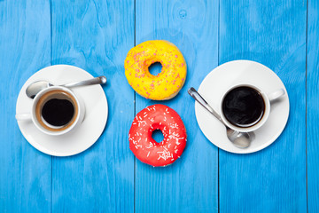 Two cups with coffee and donuts on a blue wooden table