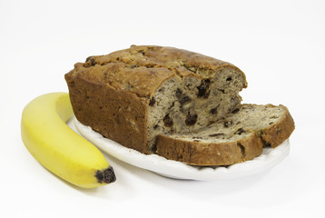 Homemade banana bread with raisins on a white dish with a banana against a white background.