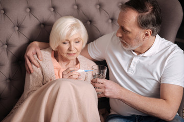 Elderly lady checking thermometer near husband