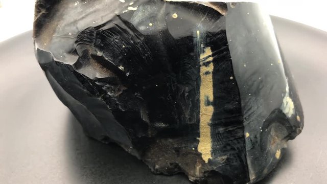 Rotating big piece of black Obsidian, a natural volcanic glass with black background.