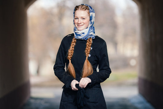 Young beautiful fashionable redhead woman with braids hairdo in blue white headcraft stylish denim black trench jacket posing outdoors in street arc spring time