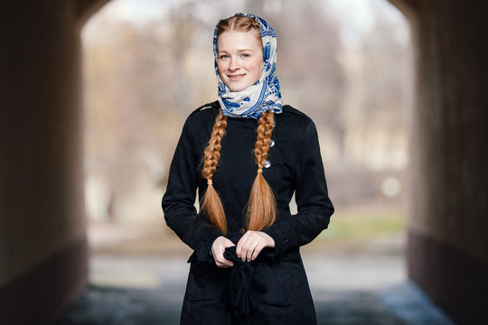 Young beautiful fashionable redhead woman with braids hairdo in blue white headcraft stylish denim black trench jacket posing outdoors in street arc spring time
