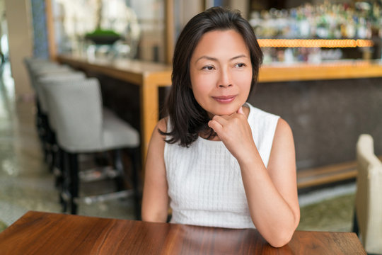 Elegant Asian middle-aged businesswoman pensive portrait. Beautiful mature Chinese business woman relaxing in restaurant bar urban stylish living in Shanghai, China. Mindfulness concept.