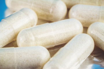 White capsules of glucosamine chondroitin, healthy supplement, pills on blue glossy background, macro image.