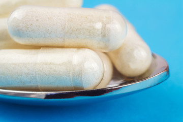 White capsules of glucosamine chondroitin, healthy supplement, pills in the spoon on blue background, macro image.
