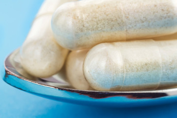 White capsules of glucosamine chondroitin, healthy supplement, pills in the spoon on blue background, macro image.