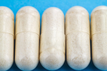 White capsules of glucosamine chondroitin, healthy supplement, pills on blue background, macro image.