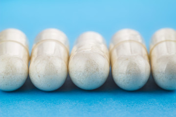White capsules of glucosamine chondroitin, healthy supplement, pills on blue background, macro image.