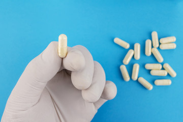 Hand in medical glove keeps one white capsule of glucosamine chondroitin, healthy supplement, pill on blue background, macro image.