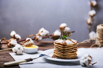 Fototapeta na wymiar American pancakes on a plate with mint, caramel, syrup, love sign and sugar powder. With the cotton branch on a back and a copy space.