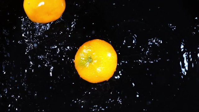 Two mandarines are falling and splashing in extreme slow motion. Shooting with high speed camera. Overhead top view.
